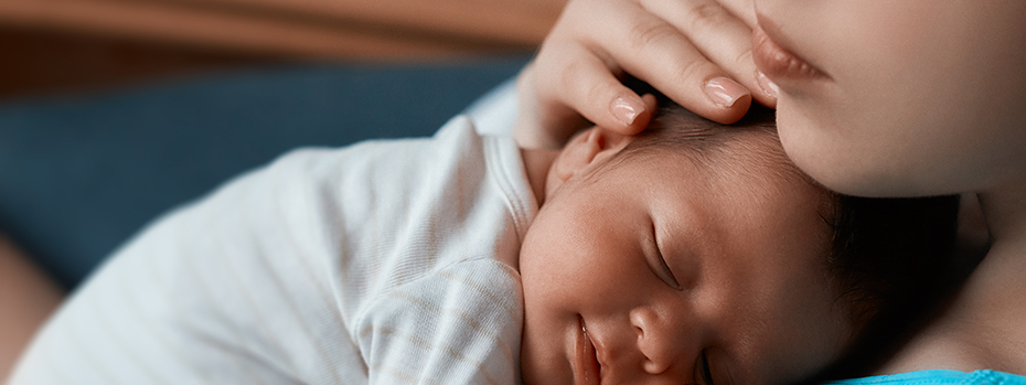 A newborn baby smiles while sleeping, held close by their parent.