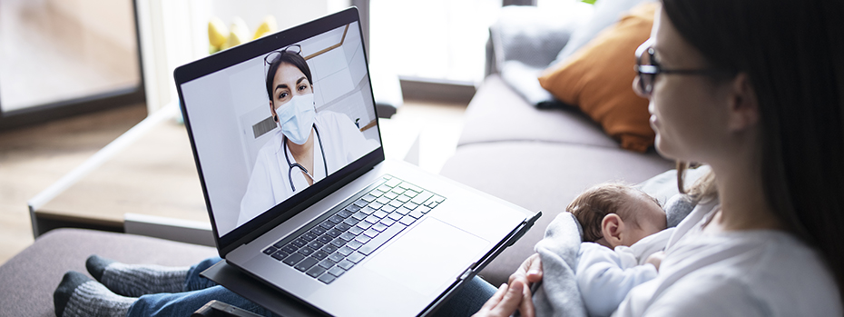 A mom snuggles her newborn while talking with a provider on her laptop.
