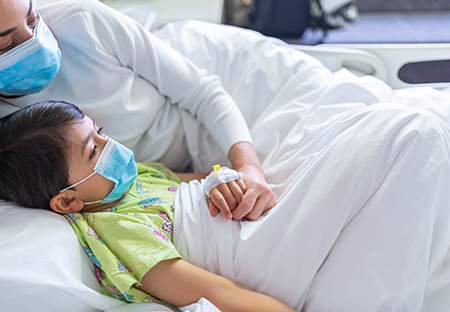 A young patient rests in a hospital bed with his parent.