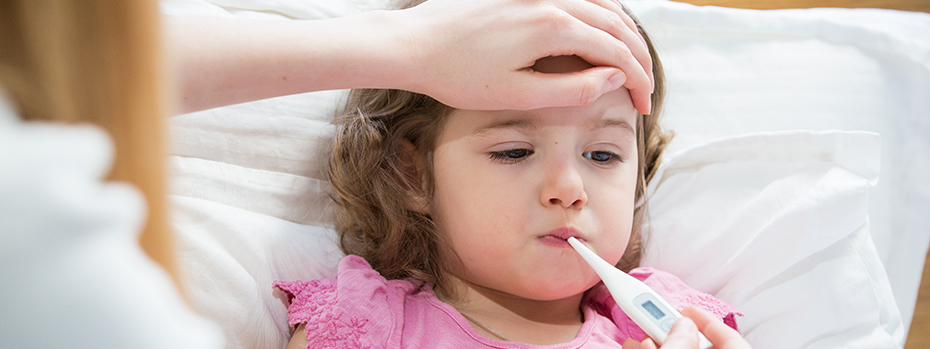 An adult puts a hand on a child’s forehead while taking her temperature with a digital thermometer in her mouth.