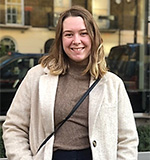 A woman smiling on the street in front of a building.