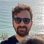 A man wearing sunglasses outside with a body of water in the background.