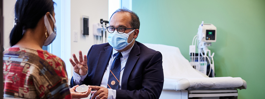 Dr. Rocha explains to a woman patient how an HAI pump works. She holds a sample HAI pump in her hand, and he is gestures as he speaks.