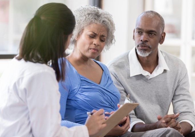 Female doctor has a serious conversation with an older couple who look very concerned.