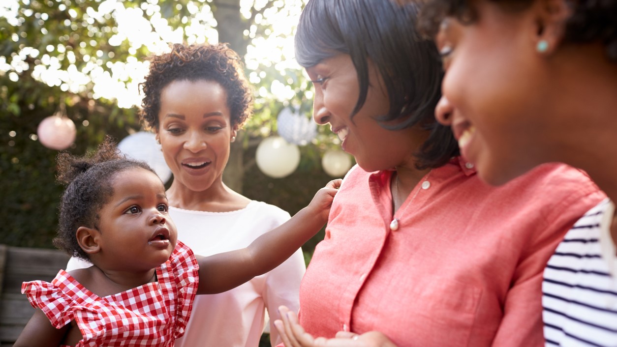 Three generations gather outdoors, smiling at one another.