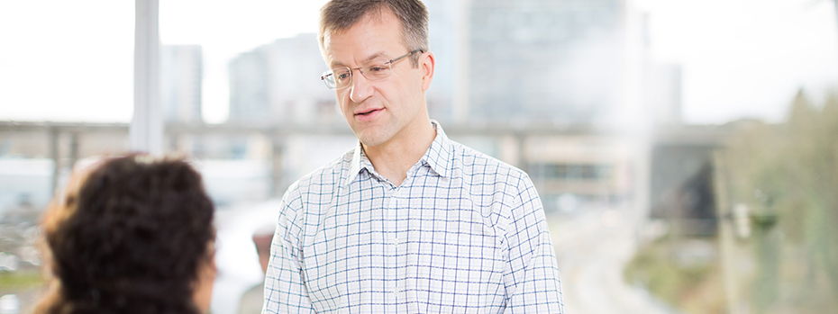Dr. Charles Henrikson speaking to a seated female patient with Portland's South Waterfront visible through the window behind him.