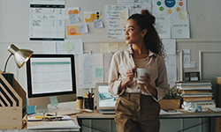 A woman stands in an office holding a coffee mug.