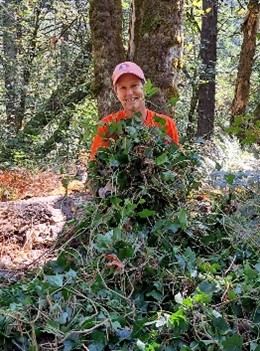 Juliet Baker in orange shirt and pink hat surrounded by trees.