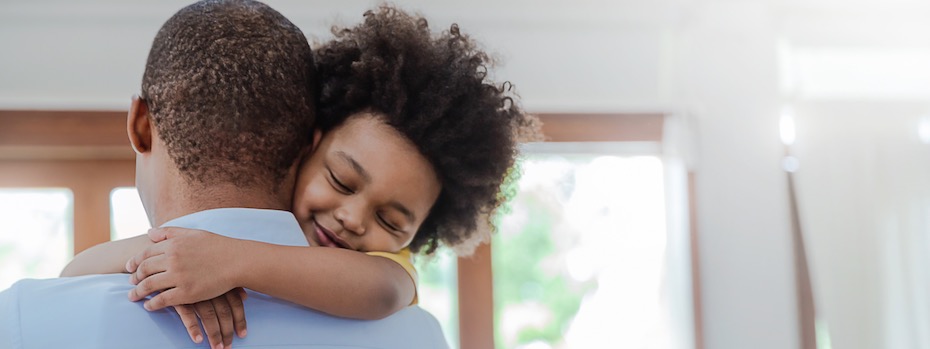 A smiling child embraces an adult.