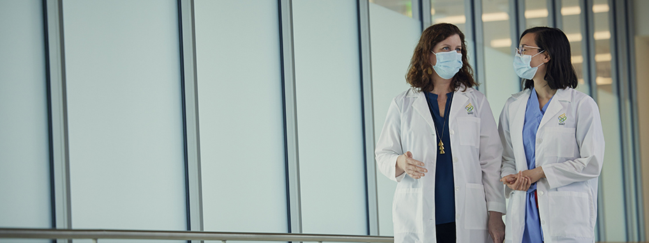 Dr. Baldwin and Dr. Wong chat as they walk through a hallway in Kohler Pavilion.
