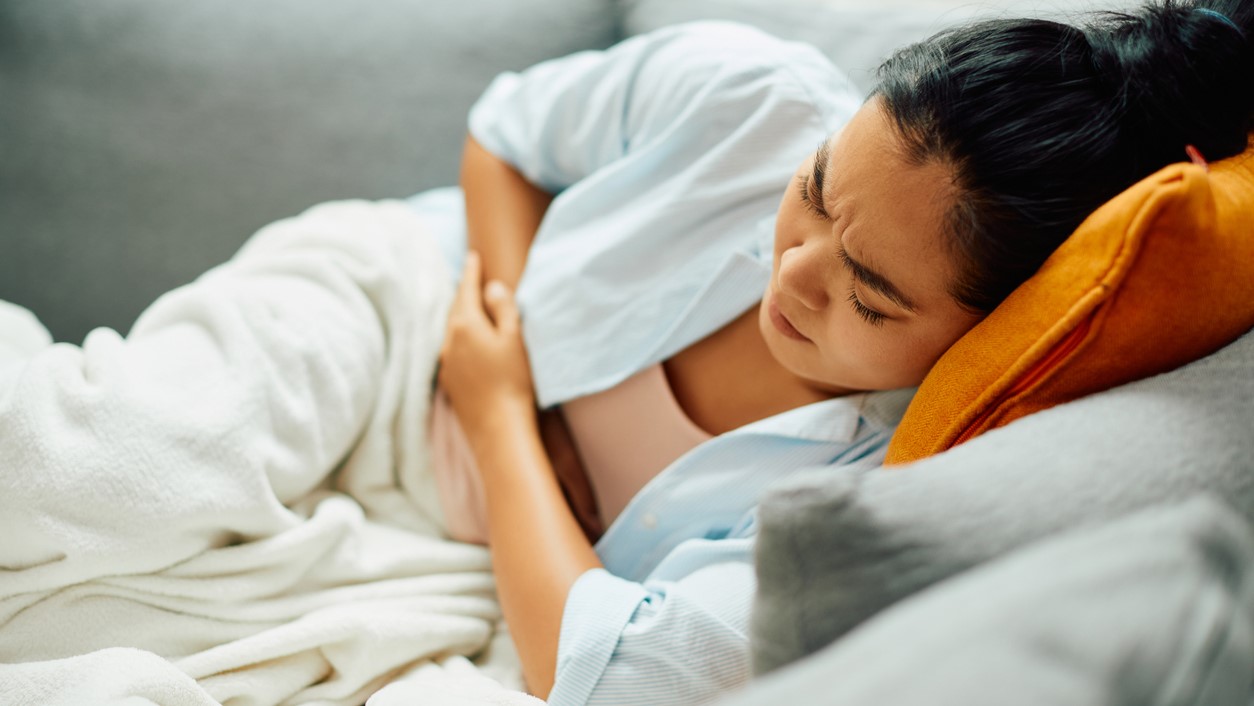 A person lays on a couch, grabbing their abdomen in pain.