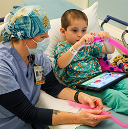 An 博彩网站 child life therapist keeps a child company while he plays with a toy before spine surgery.