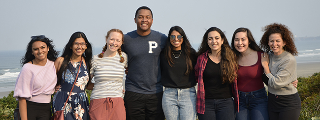A group of doctors in casual attire standing next to each other smiling at the beach.
