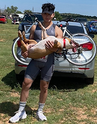 A man standing on grass on a sunny day holding a dog.