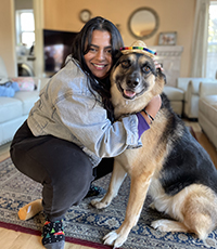 A woman smiling crouching down and hugging a dog.