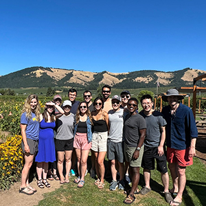 A group poses in a field of flowers with low hills in the background.