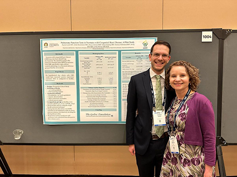 A man and a woman stand in front of a research poster smiling.