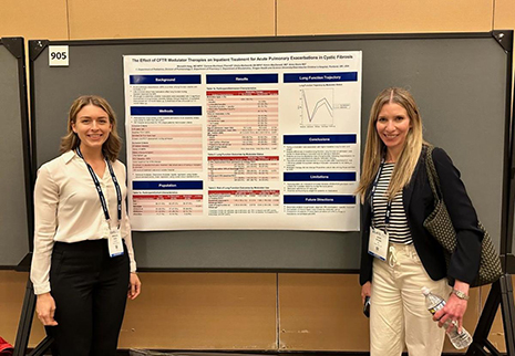 Two women standing on either side of a research poster smiling.