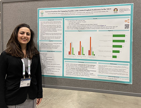 A woman smiles while standing next to a research poster.