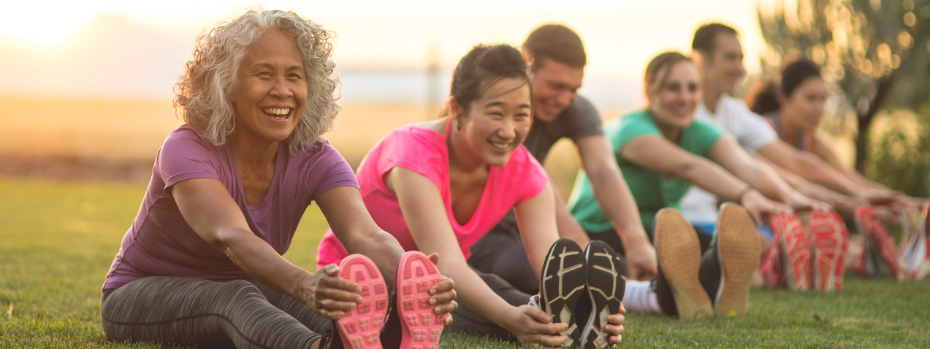 Several multigenerational peers sit on grass while stretching their legs