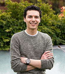 Lab assistant Tyler Ramos smiles at the camera while standing in front of a green tree