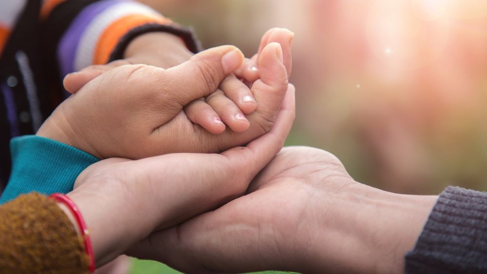 Four hands of different ages stack up against a blurred, bright background.