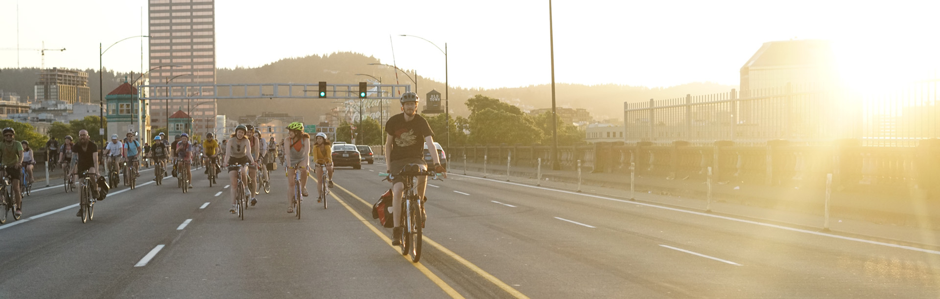 A group of people bike over the Burnside Bridge at sunset.