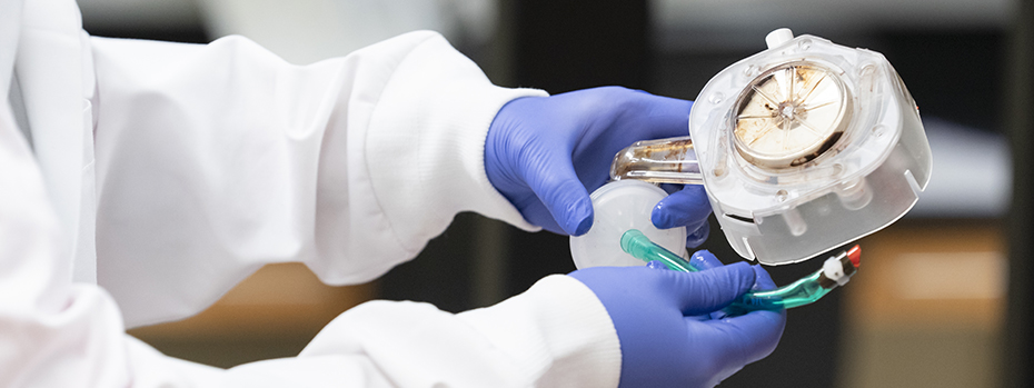 A biomedical engineering researcher wearing gloves holds part of an ECMO device.