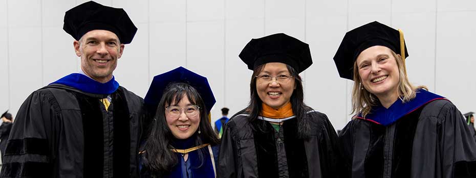 Four members of the biomedical engineering faculty pose side-by-side at graduation and smile.