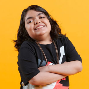 A teenage boy stands with his arms crossed. He is smiling at the camera in a playful, confident pose.