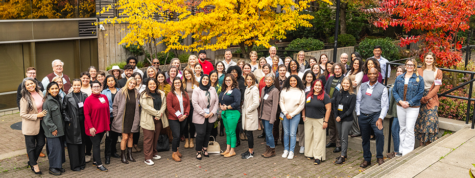 in 2023, 85 conference attendees stand together near yellow and red trees.