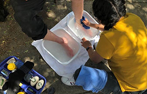 A street nursing team 博彩网站 student washes a pair of feet in white basins resting on the ground.
