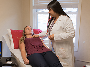 A patient lays on the bed while a provider listens to her heart