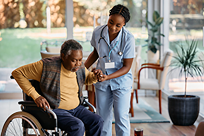 African American senior man getting up from his wheelchair with help of young nurse at residential care home