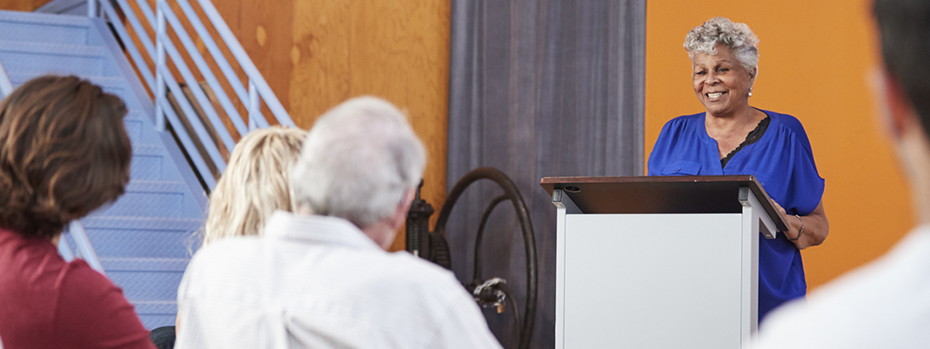A woman speaking at a podium to a seated audience.
