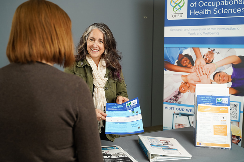 OccHealthSci exhibition table with people taking materials.