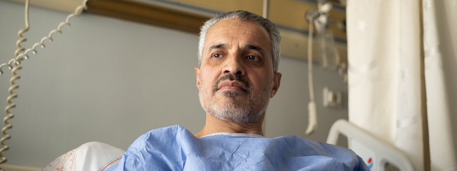 A male patient wearing a hospital gown lies in a hospital bed.