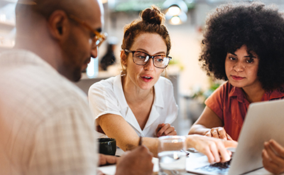 Business women having a work lunch in a café, exchanging ideas and discussing their projects with a client. Young business team using a laptop as they sit around a coffee table.