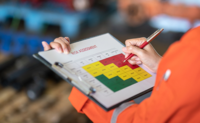 Action of a person is using ballpoint pen to marking on the risk assessment matrix table at "High risk" level.