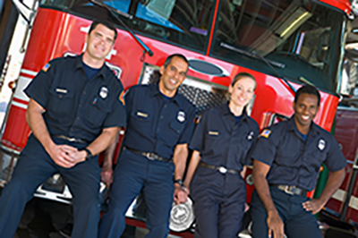 Several firefighters sitting on the bumper of a fire engine.