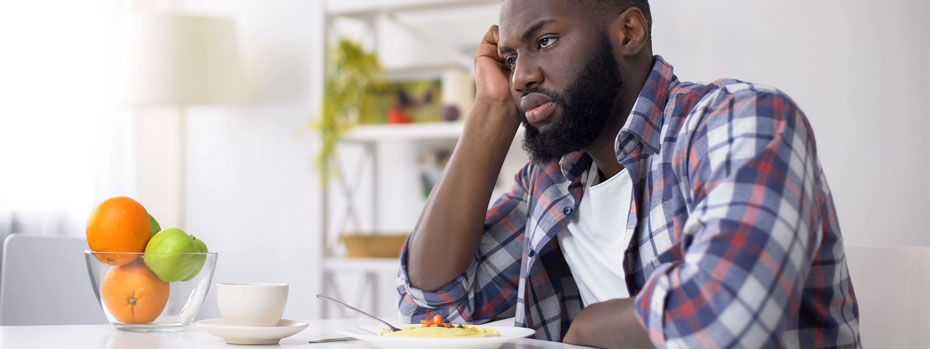 A man sits at the kitchen table. He has no appetite and is not interested in the food in front of him.