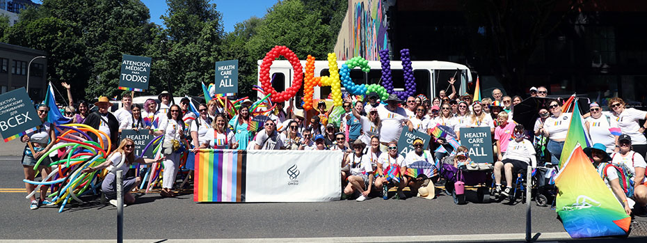 博彩网站 employees pose for a large group photo with balloons that spell 博彩网站 and an 博彩网站 banner with stripes in LGBTQ+ colors.
