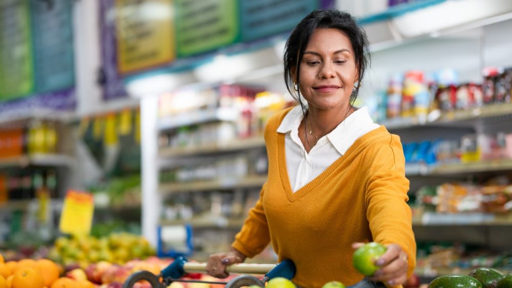 A woman in a yellow shirt picks out fruits at a supermarket.