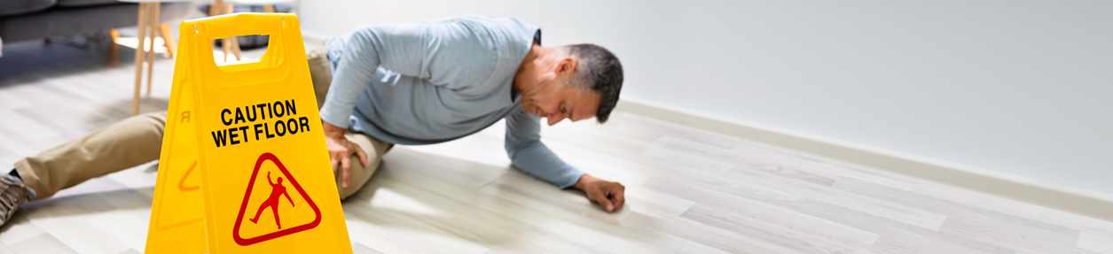 Mature Man Falling On Wet Floor In Front Of Caution Sign