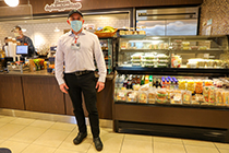 An 博彩网站 employee wearing a face mask stands in front of a coffee bar and food display case.