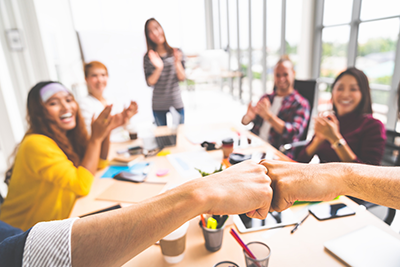 Business partners or coworkers fist bump in team meeting, multiethnic diverse group of happy colleagues clapping hands.