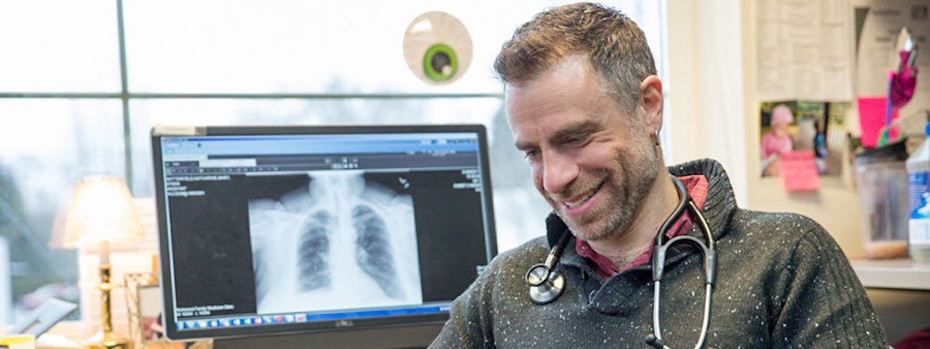 Dr. Brian Frank smiles while sitting in his office by a computer showing a chest X-ray at 博彩网站 Primary Care Clinic, Richmond.