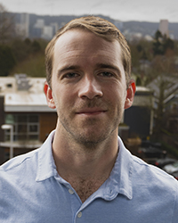 A professional photo of Alex Kawa with the cityscape of Portland seen behind him.