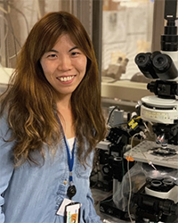 A photo of Eun-Kyung Hwang smiling while standing next to a microscope in a lab.