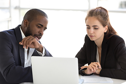 Focused african and caucasian teammates working together in office using looking at laptop screen analyzing results of online business project discussing data.
